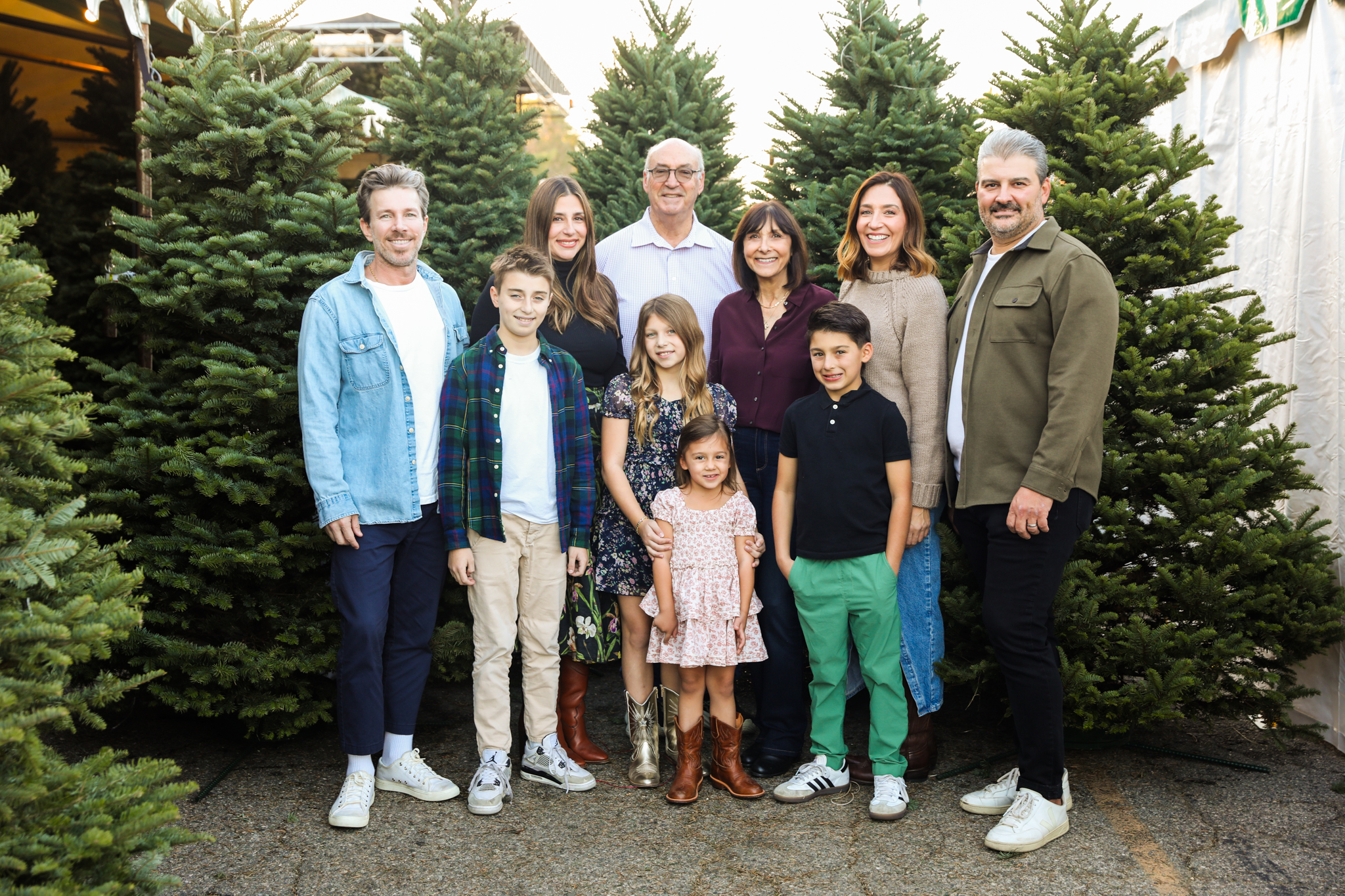 A multigenerational family gathered among Christmas trees at Tina’s Trees